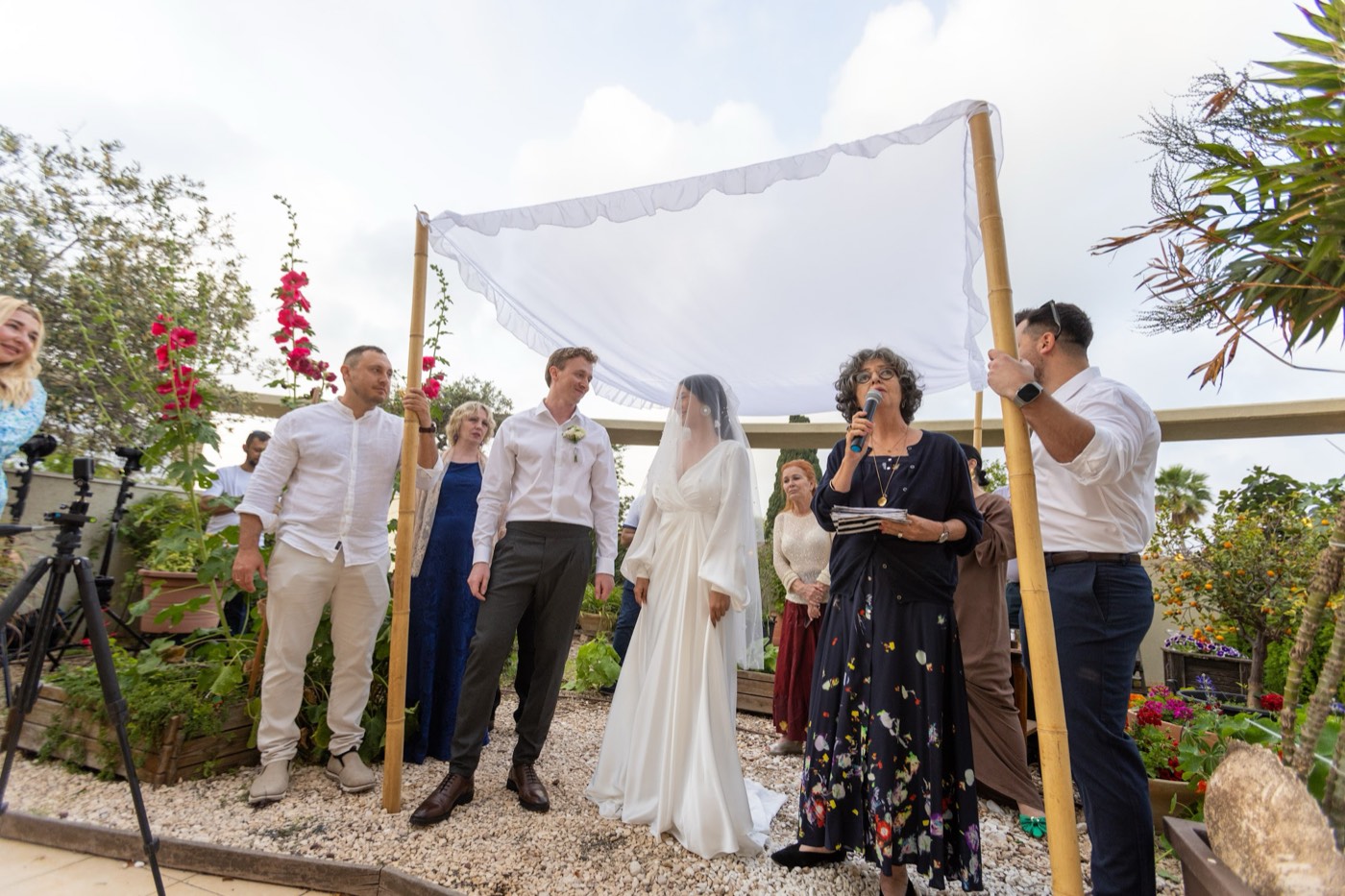 חופה של ארבעה מקלות במבוק ובד לבן, נישאת בידי ארבעה אנשים בחתונה בגן